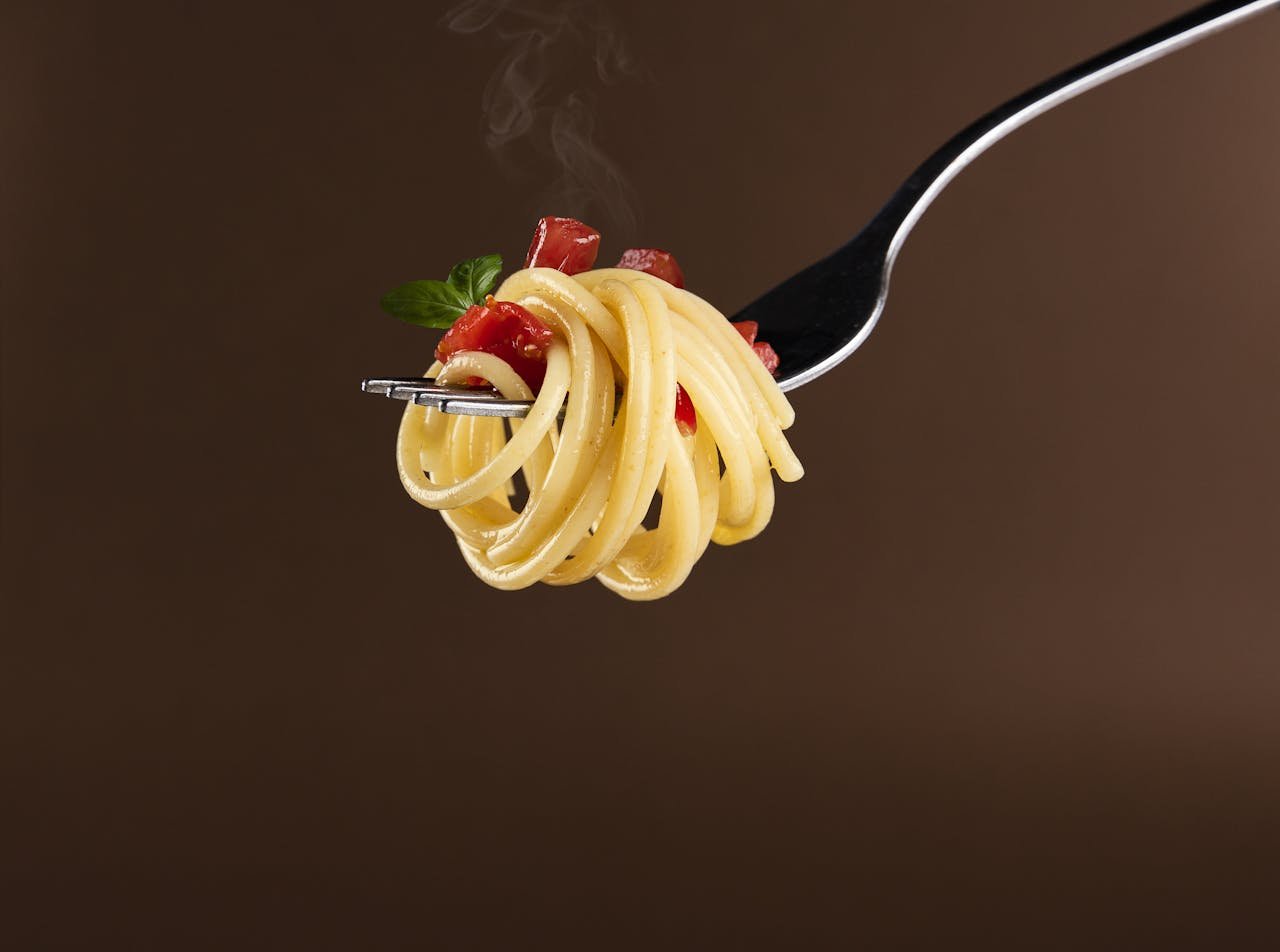 Close-up of spaghetti with tomato and basil garnish on a fork against a brown background.
